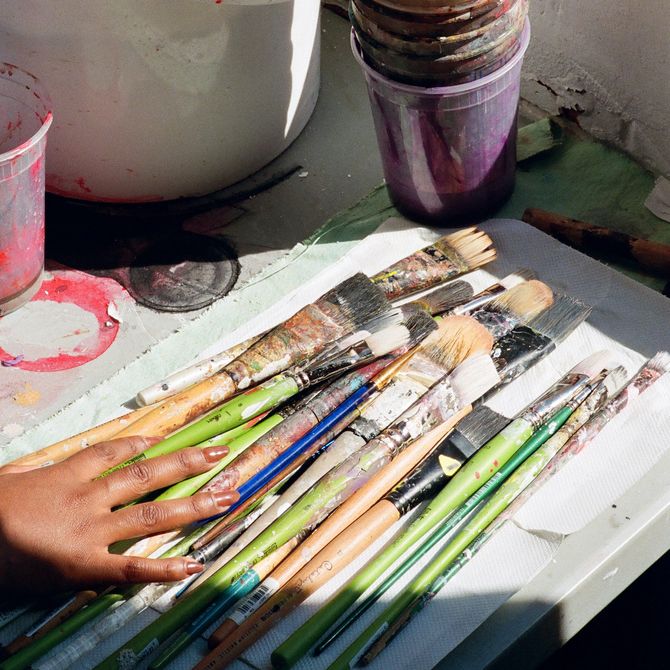 hands reaching for a pile of paint-covered brushes and a stack of plastic cups, also paint-covered