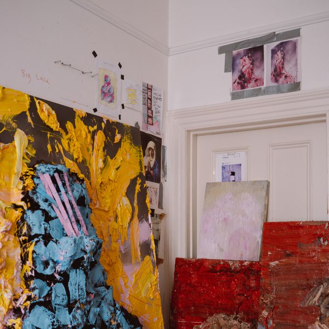 A large yellow and blue textured painting leaning against a wall, accompanied by a small red painting to it's lower left