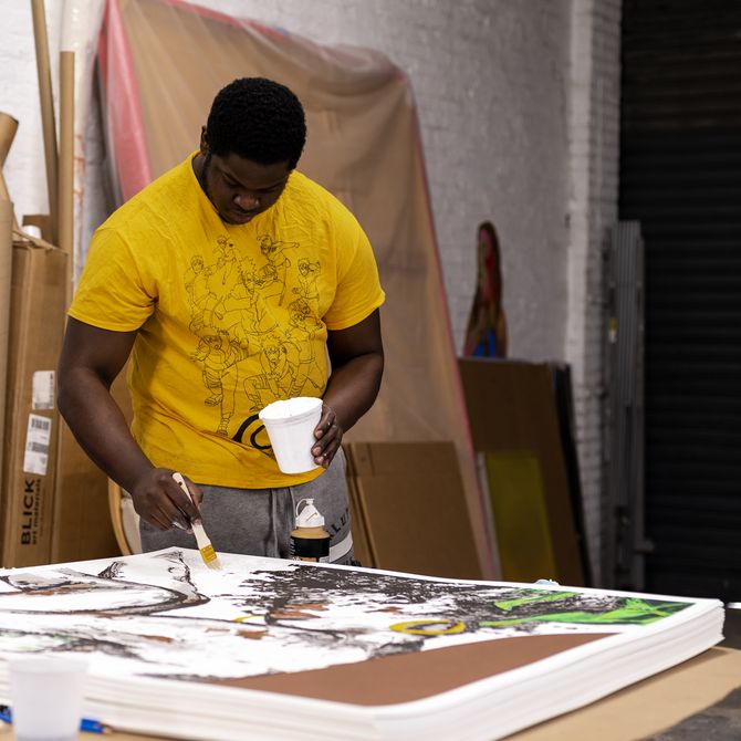 Khari Turner applying paint from a pot to a pile of prints in his studio