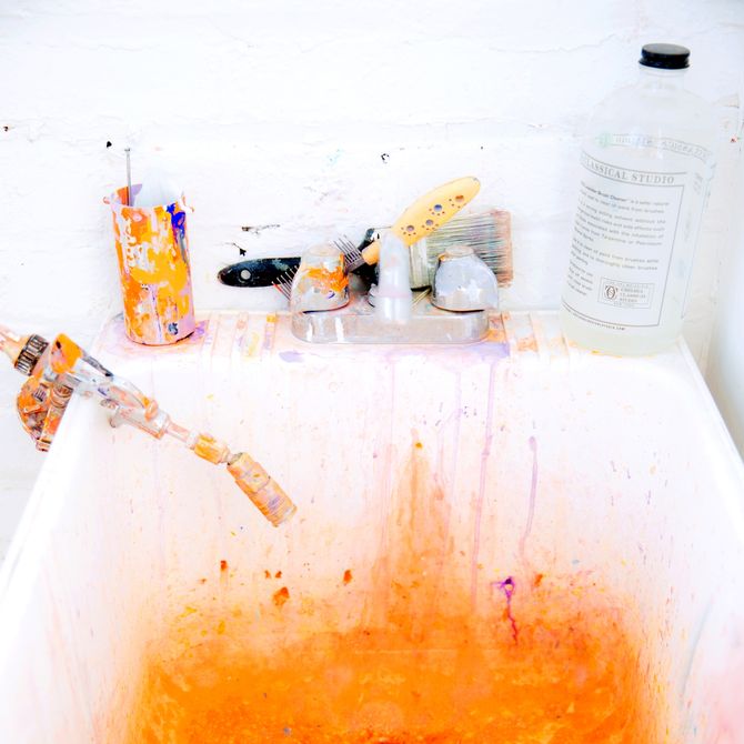 a white tub stained with orange paint with paint pots and tools on the rim