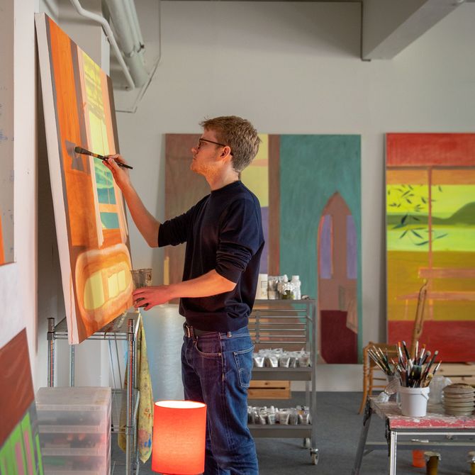 Alfie Caine paints in his studio next to warm lamp