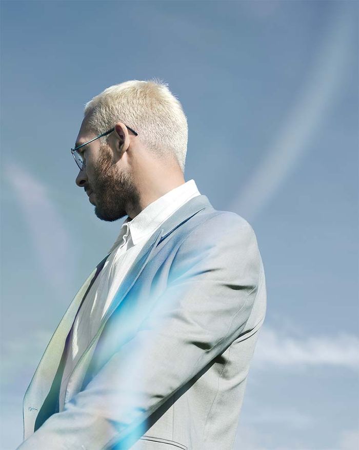 Homme devant un ciel bleu regardant au loin, portant The Wave avec des branches vert foncé