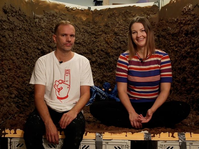 two artists sitting inside an installation made out of soil and looking into the camera