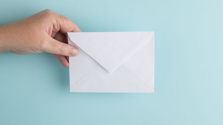 A picture of a white envelope being held in a hand against a light blue backdrop.
