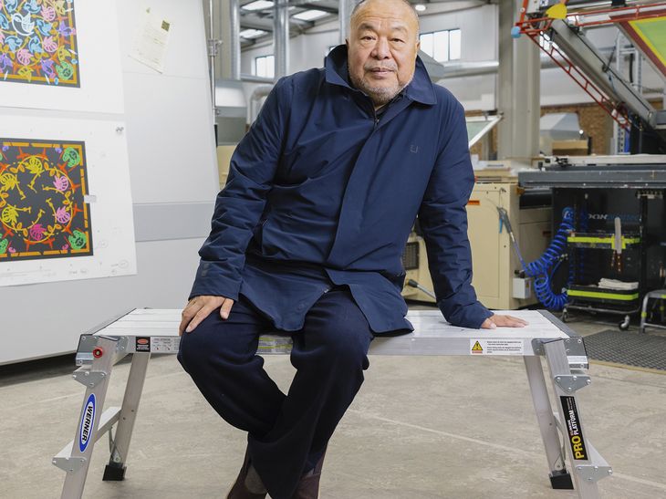 Ai Weiwei sitting on a metal bench, supporting himself with his left arm