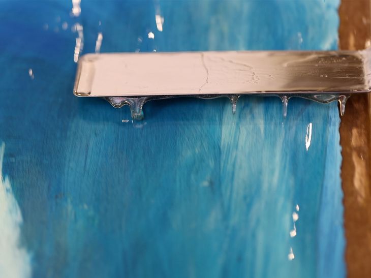 metal spatula spreading viscous resin over the surface of a vibrant blue print