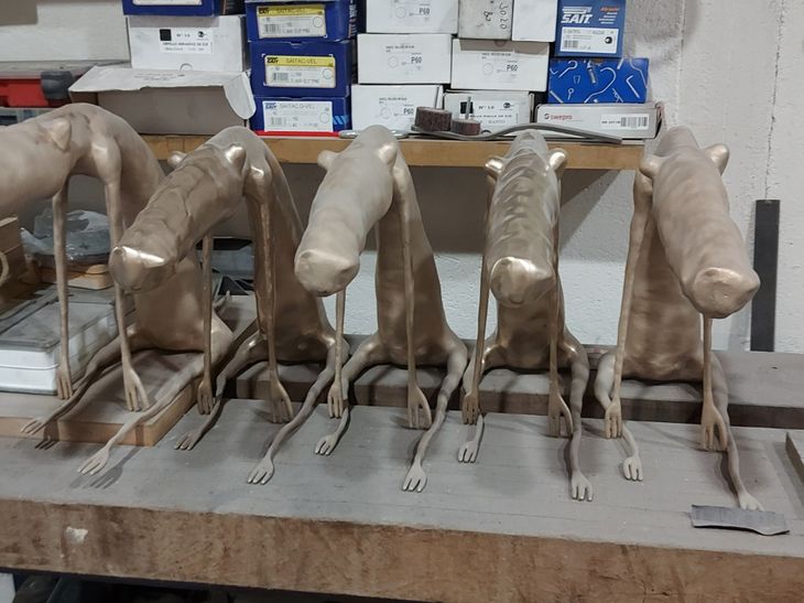 five bronze large dog sculptures in a row on a work-surface