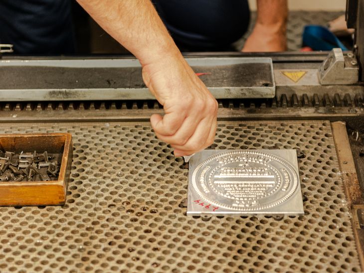 a hand adjusting a metal debossing plate in a workshop space