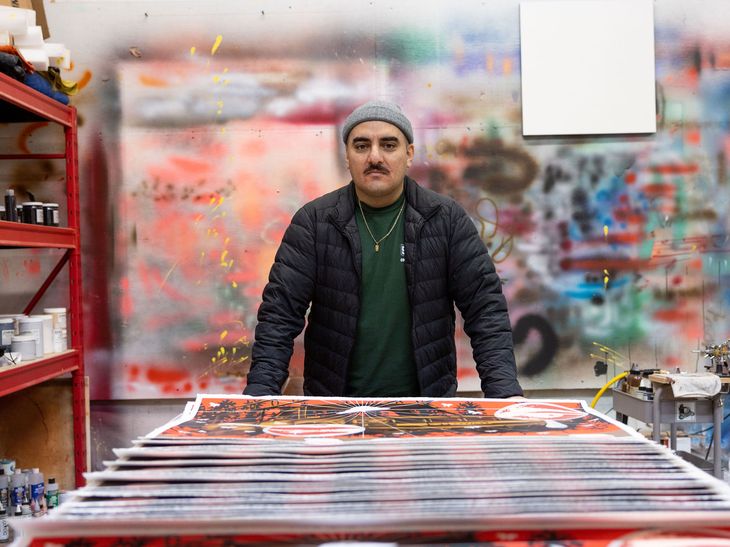 the artist Jaime Munzo stood leaning over a surface with a pile of his prints on it