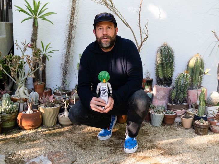 Darren Romanelli crouching holding Cactus Man figurine