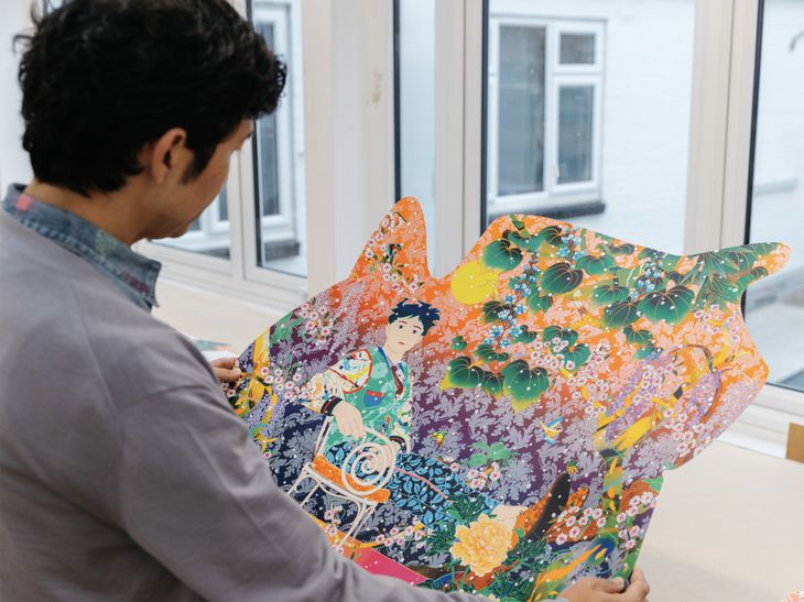 artist wearing a grey cardigan, inspecting a finished, custom-shaped, vibrantly-coloured screenprint