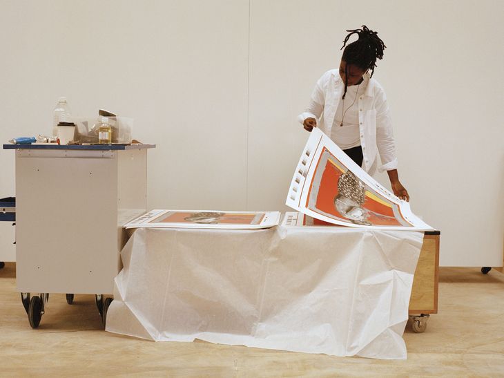 artist inspecting the top print from a stack resting on a low table