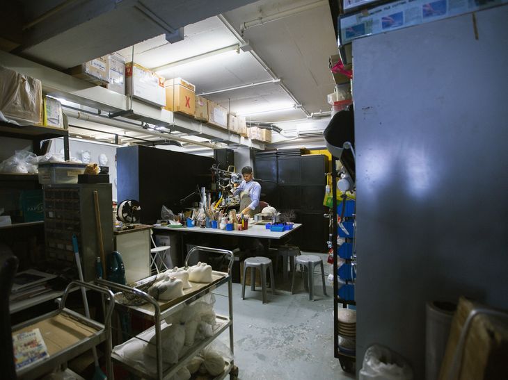 johnson tsang at work at a table in his studio surrounded by shelves, storage units and his artwork