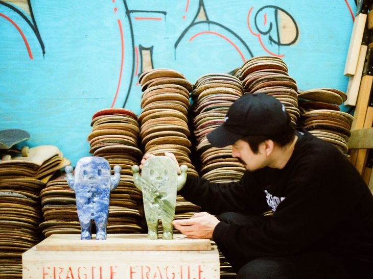 artist Haroshi kneeling down to look at two GUZO sculptures