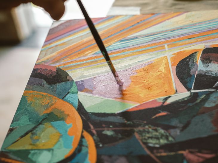 close-up of a paintbrush applying layers of violet paint to a colourful geometric print