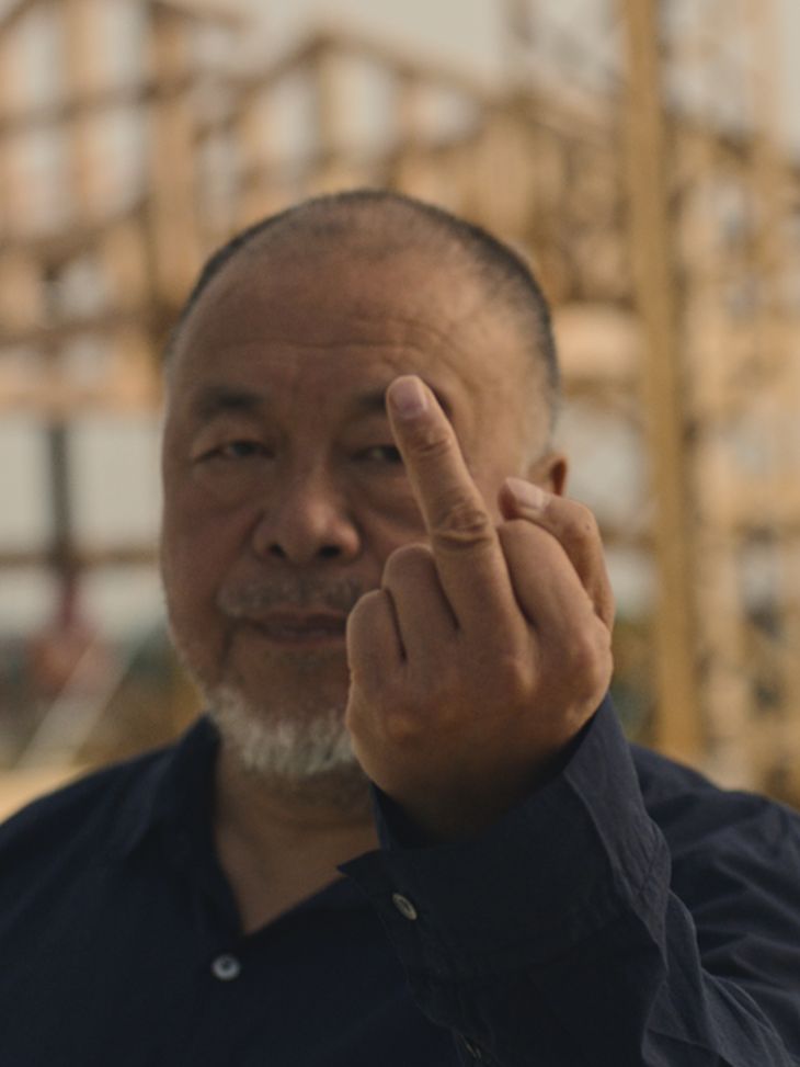 Ai Weiwei raising his middle finger to the camera with a serious expression