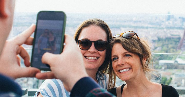 two women taking a selfie with the Eiffel tower in the background in France