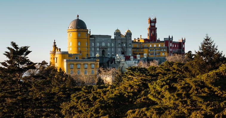 yellow purple and red pena palace surrounded by lush trees in sintra portugal