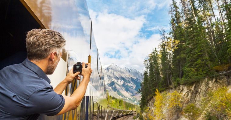 man looking out window of a train taking a photo of the swiss alps