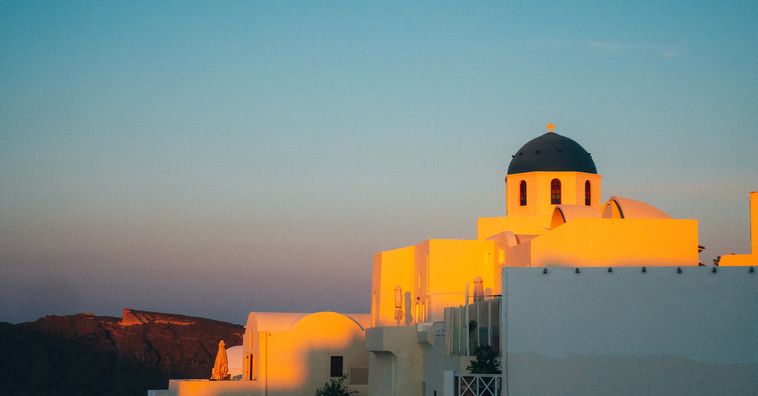 white domed building in greece with sun shining on it