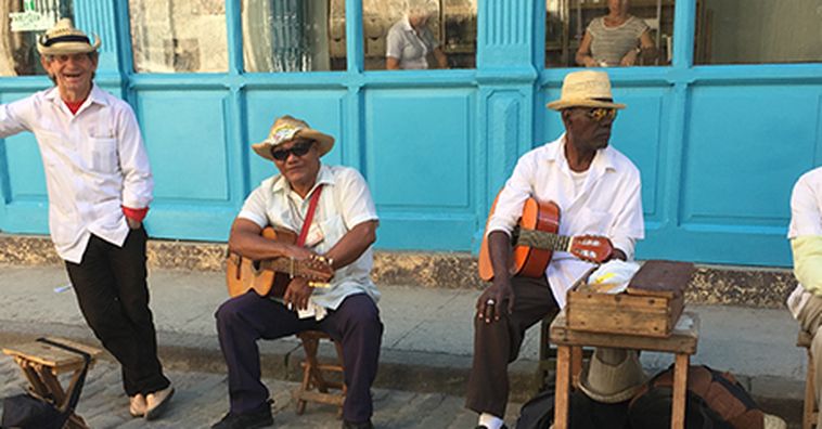 four cuban musicians sitting outside a bright blue building in havana