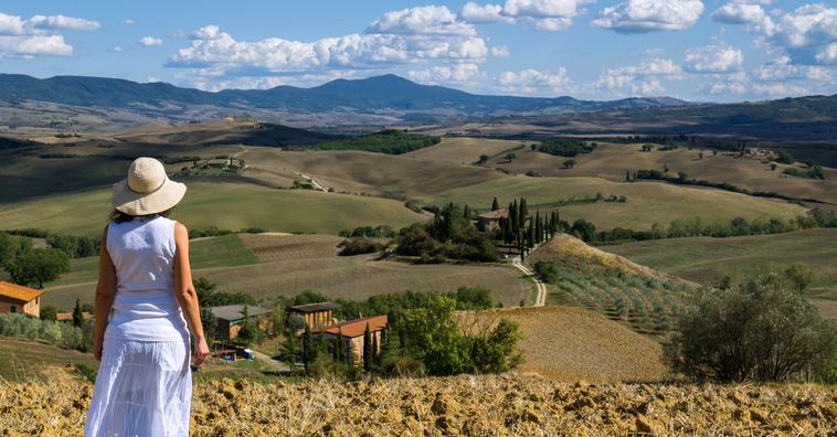 woman with a hat standing in the grass looking at the rolling hills in tuscany italy