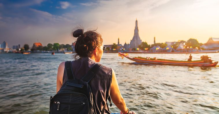 woman wearing sunglasses looking across the river in bangkok with boats floating by