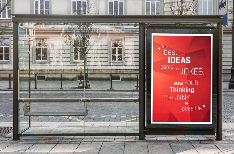 Bushaltestelle mit Plakat mit Aufschrift "Best ideas come as jokes. Make your thinking as funny as possible."