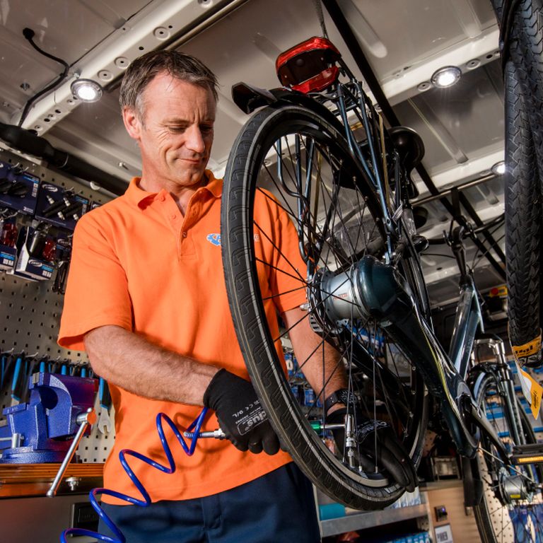A bike mechanic is inflating the tire of a bicycle.