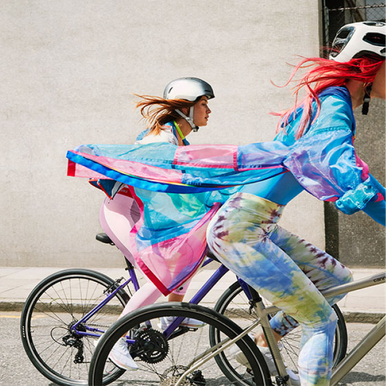 Two woman wearing colorful coats, cycling on a Cannondale bike in an urban surrounding