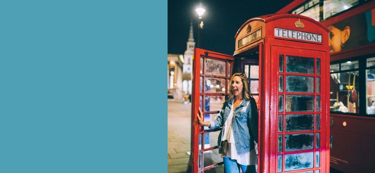 A woman traveler steps out of one of London's famous red phone booths with a big smile on her face.