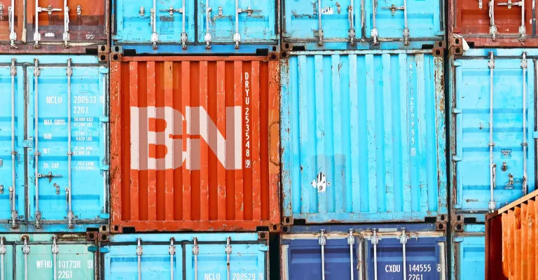 Side view of different stacked colorful shipping containers with the B+N logo printed in white on an orange one.