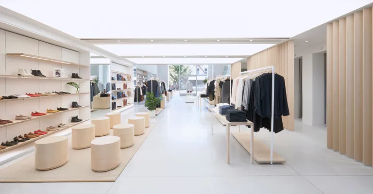 Interior view of Evelane's shop. A white space is decorated with wooden seats and tables with wooden System 1224 shelves lining against the left wall to display pairs of shoes.
