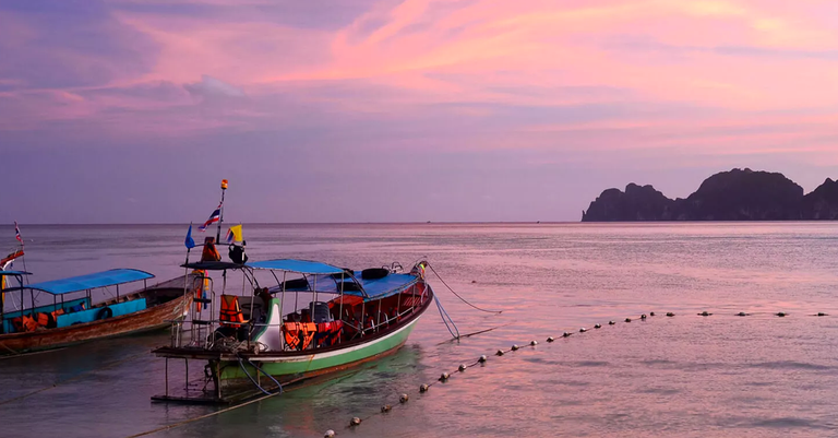 A boat sitting in the calm ocean waters of Thailand during sunset.