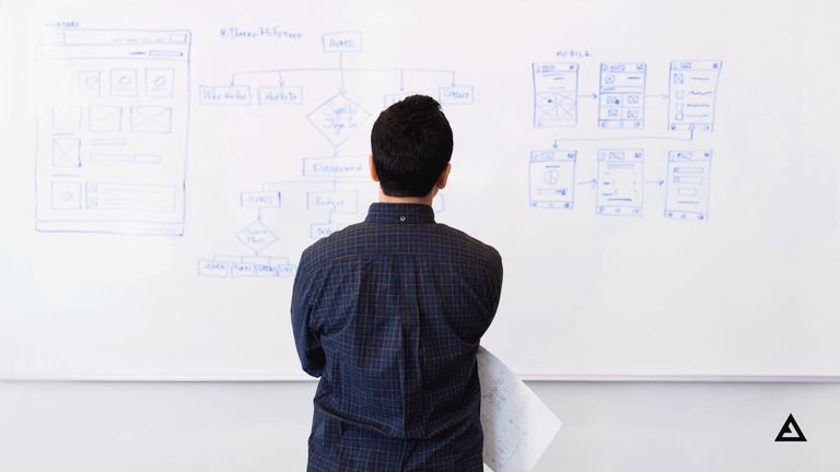 A man stands in front of a whiteboard that has product drawings drawn on in blue ink