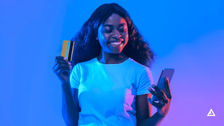 A girl holds a credit card in one hand and a phone in the other.