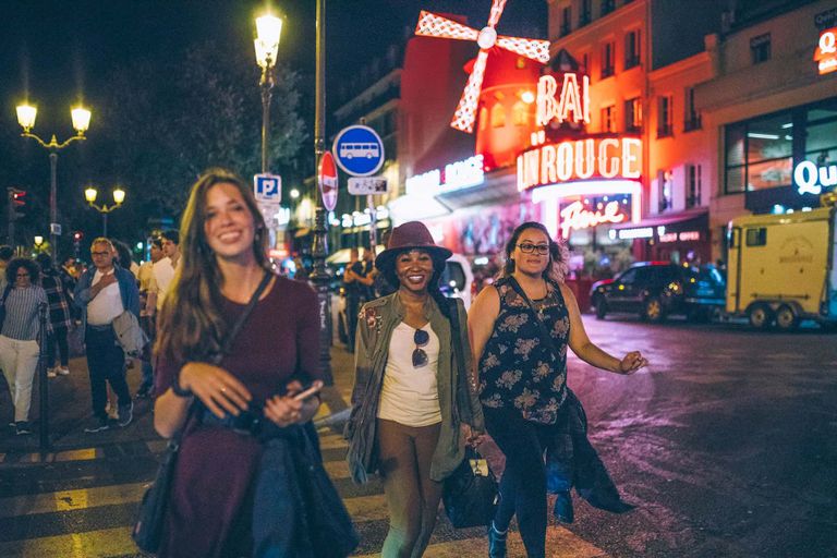 Three female travelers walking down a lively street at night somewhere in Europe.