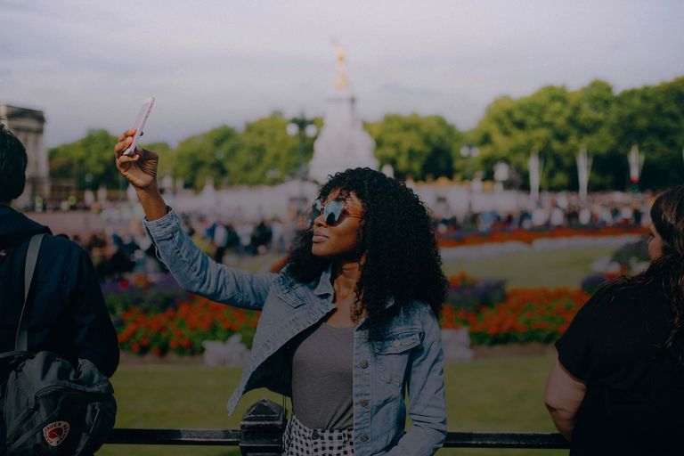 A woman traveler takes a selfie in front of the gardens at London's famous Buckingham Palace.