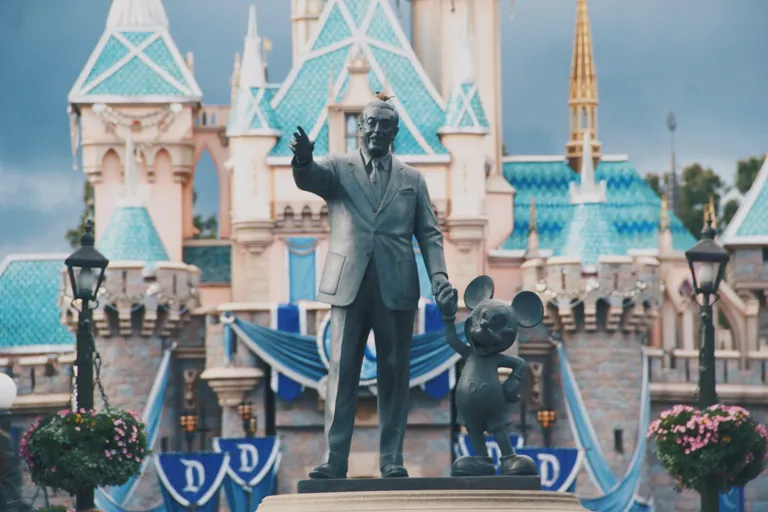 A statue of Walt Disney and Mickey Mouse in front of the Disney castle