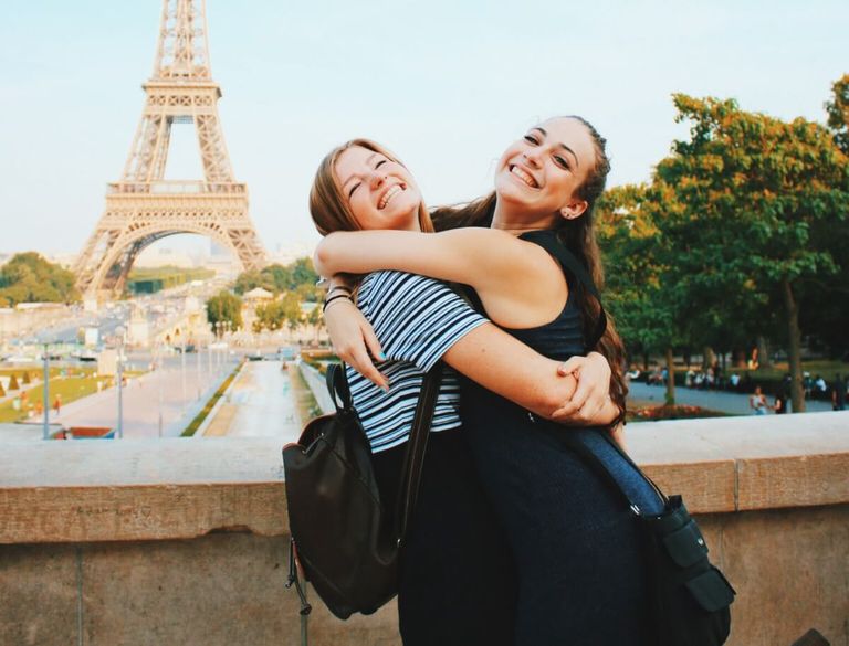 Two girls hugging in front of the Eiffel Tower.