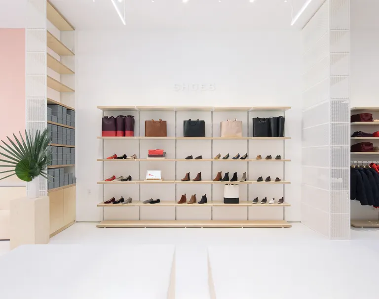 Wooden System 1224 shelves along a white wall are used to display various shoes and purses on sale.