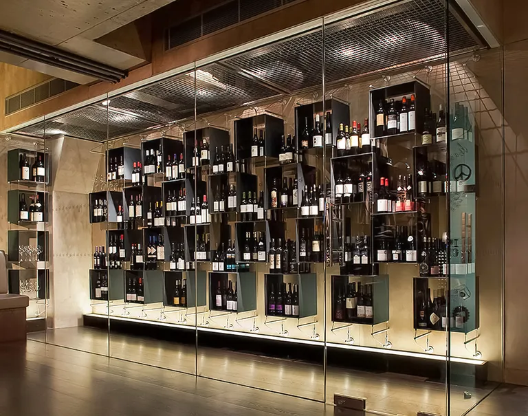 View of a large glass display showcasing a variety of wines held up on square black shelves through Cables and Rods.