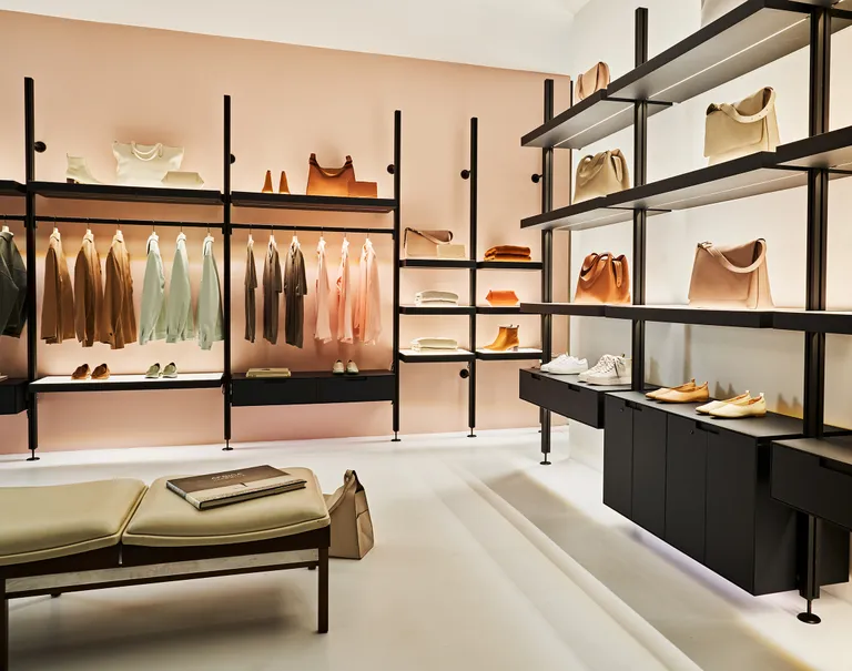 Lit black Sorbetti shelves are lined against the walls of a retail store. The system shelves various bags and shoes on display as well as clothes hung on the racks.