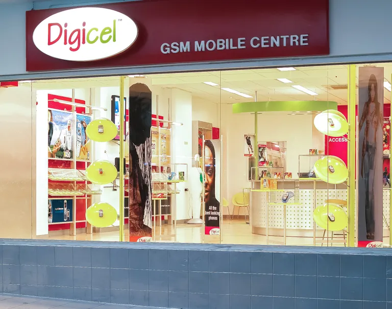 Exterior of a Digicel store's entrance. The Digicel logo is lit up above glass windows showing the interior of the store.