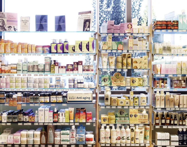 Many different beauty products are placed along a series of glass shelves against a bright window.