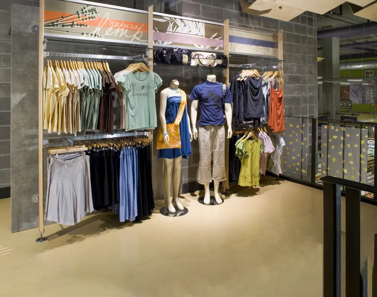 Clothing items are hung up on display on wooden and metal racks. Two mannequins wearing clothes are placed in the center.