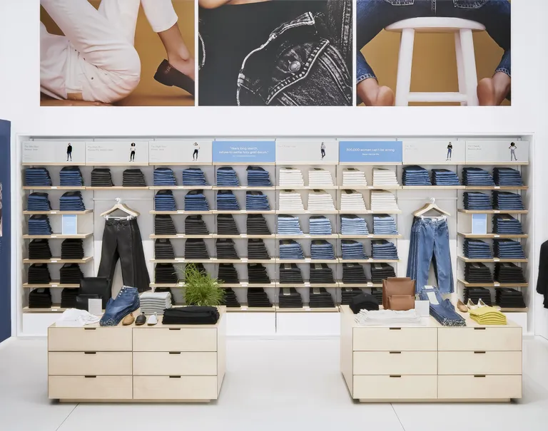 Various clothing items, mainly jeans, are neatly folded and on display within wooden shelves against a wall.