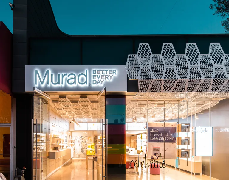 Entrance of Murad's shop with open glass doors and glass windows. The Murad logo is printed largely over the doors on top of metal, with metal embellishments on the side.