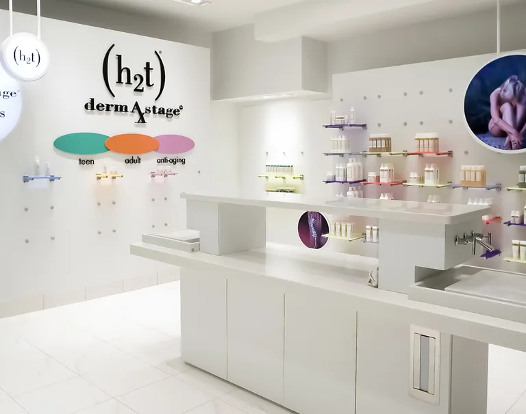 Interior of a white store. White walls using metal puck fixtures prop up colorful shelves displaying bottles.
