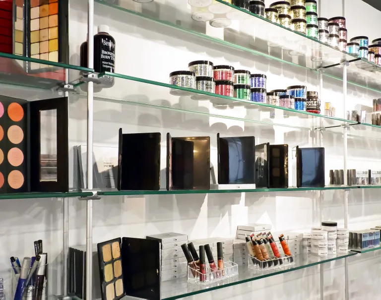 Various makeup products are lined up neatly along glass shelves held up by metal cables and rods.